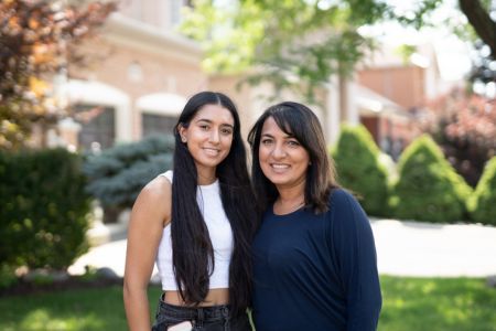 A mother and her daughter smiling in front of a house.